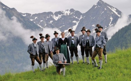 Gruppe in traditioneller Tracht auf einer Almwiese vor alpiner Berglandschaft.