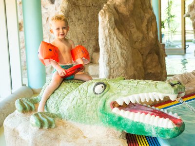 Kleines Kind mit Schwimmflügeln sitzt auf einem Krokodil-Spielzeug im Wasser.