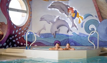 Zwei Mädchen im Whirlpool mit Delfinbild und bunter Meeresdeko.
