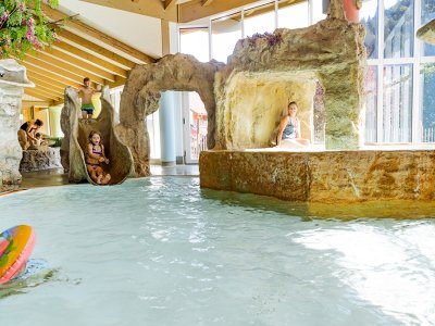 Kinder rutschen ins Hallenbad mit Felsenlandschaft und Grotte.