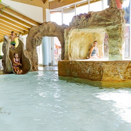 Children sliding into indoor pool with rock formations and grotto.