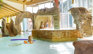 Kinder und Erwachsene in Grotte, Mädchen mit Poolnudel im Wasser.