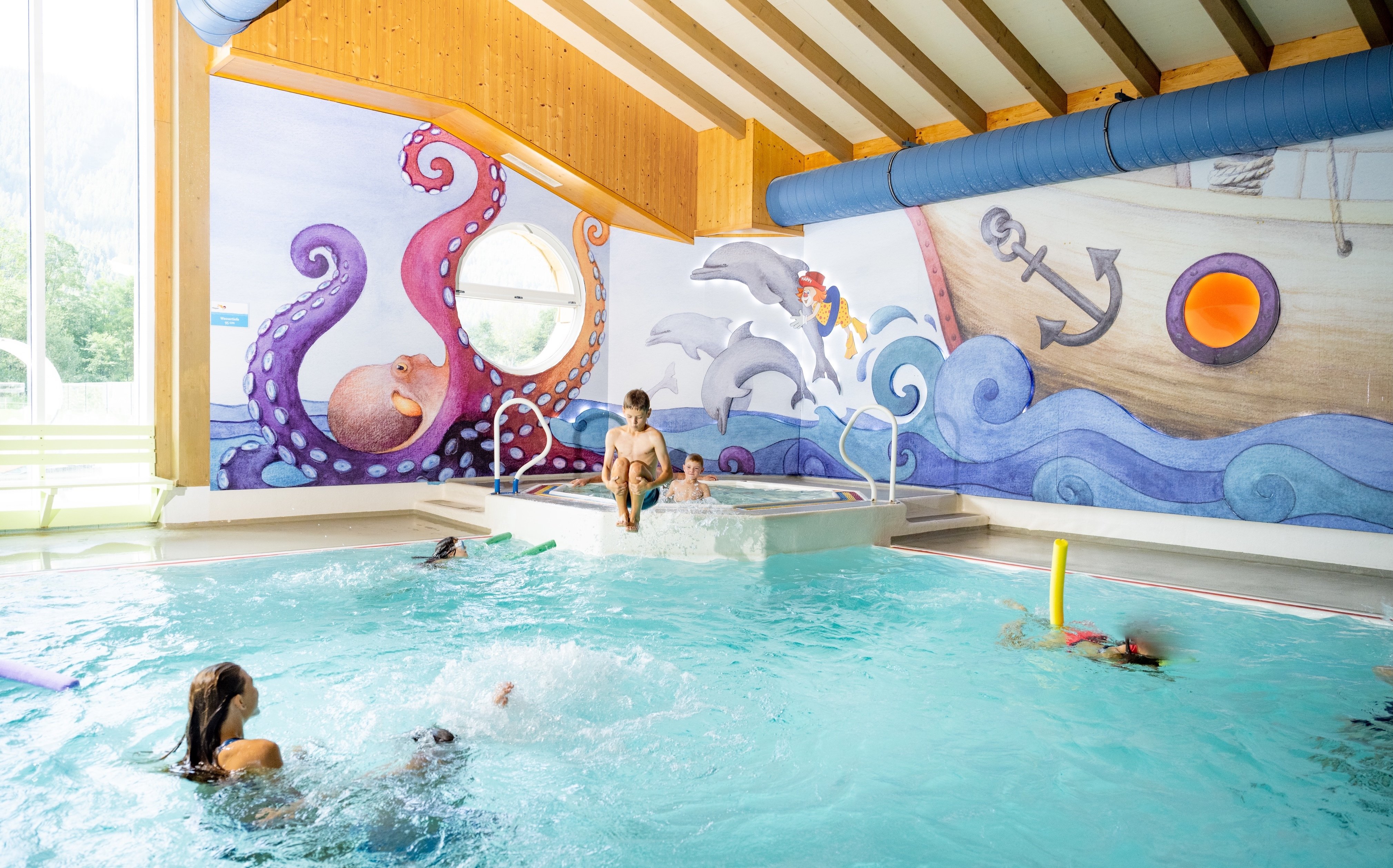 Kinder im Hallenbad mit bunter Wandmalerei im Unterwasserstil.