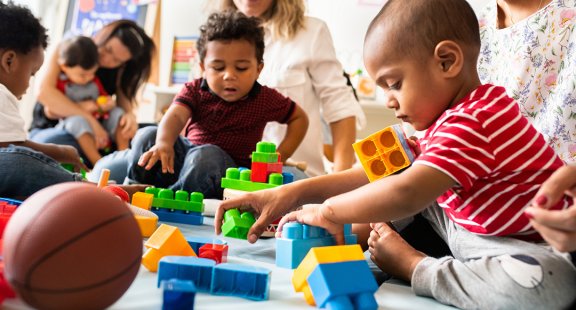 Das Bild zeigt Kinder und Erwachsene, die mit bunten Bausteinen in einem Raum spielen.