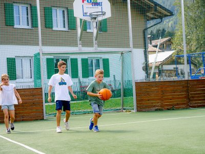 Kinder spielen Basketball auf dem Außenplatz.