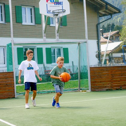 Kinder spielen Basketball auf dem Außenplatz.
