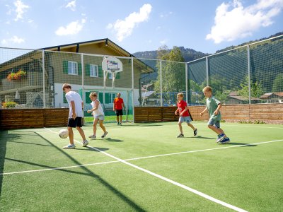 Kinder spielen Fußball auf dem umzäunten Sportplatz.