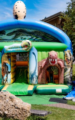 Bunte Dino-Hüpfburg mit Rutsche und großem Ei obendrauf.