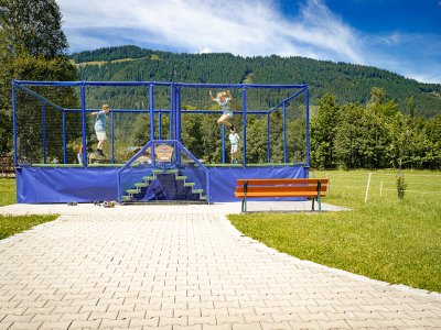 Kinder springen auf Trampolin vor Bergkulisse.