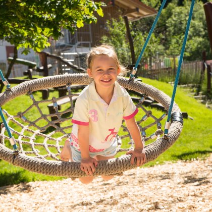 Ein Mädchen schaukelt auf einer Nestschaukel auf einem Spielplatz.
