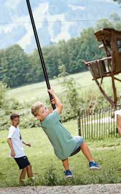 Junge fährt Seilrutsche, Kinder schauen im Waldspielplatz zu.