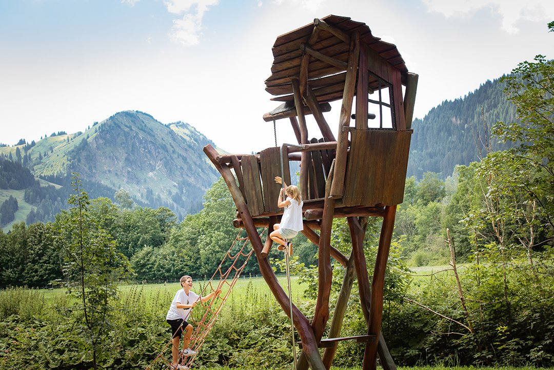 Kinder klettern zum hölzernen Baumhausturm in den Bergen.