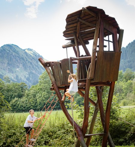 Kinder klettern zum hölzernen Baumhausturm in den Bergen.