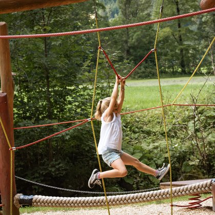 Mädchen schwingt an Seilen auf Kletterspielplatz im Wald.