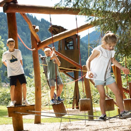 Children balancing on ropes at wooden adventure playground.