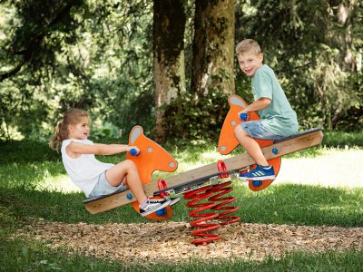 Mädchen und Junge spielen auf Wipptier im Waldspielplatz.