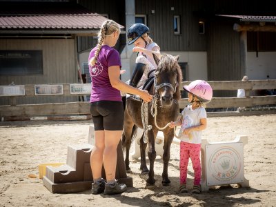 Mädchen steigt mit Hilfe aufs Pony, anderes Kind hält den Strick.
