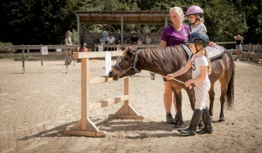 Kind auf Pony bei Spielaufgabe mit Hilfe von anderen.