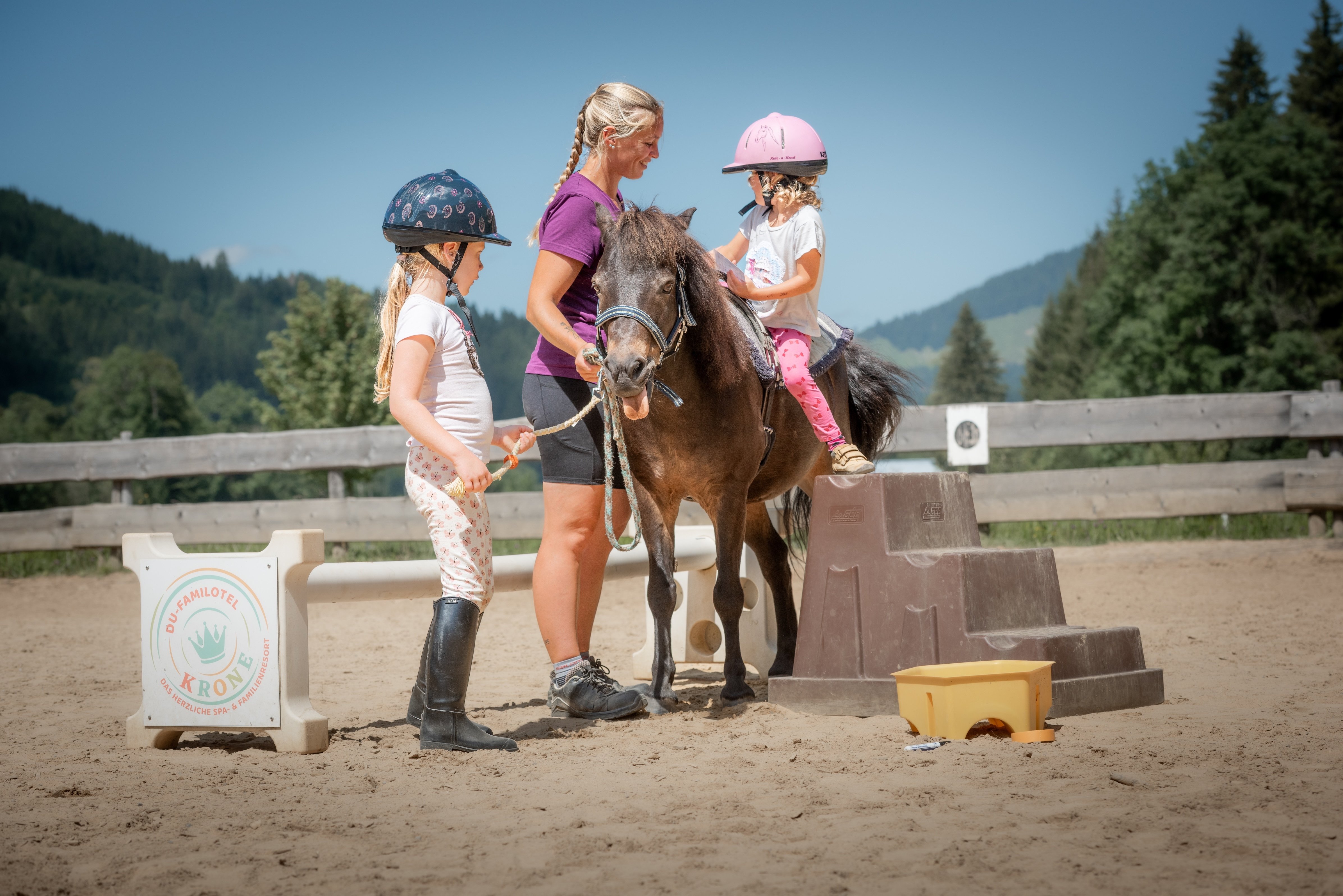 Mädchen auf Pony wird unterstützt, andere helfen vom Boden aus.